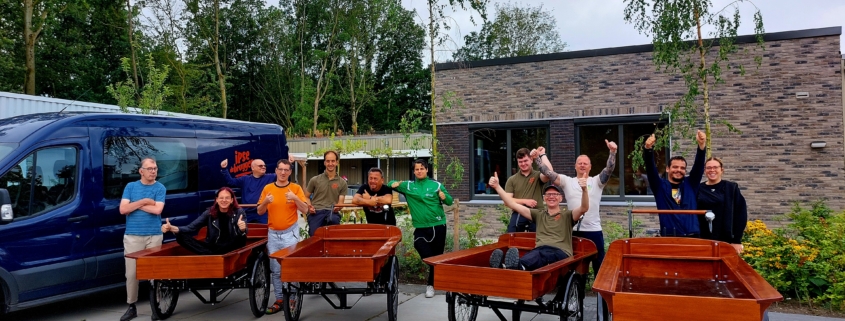 Vrolijk lachende mensen zitten op bakfietsen of eromheen en zwaaien hun handen in de lucht van geluk.